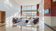Located at 29 Linden St in Hackensack, NJ, this single-floor commercial space makes an immediate impression with its grand, light-filled lobby. The entrance area boasts soaring double-height ceilings framed by exposed brick columns and an expansive wall of floor-to-ceiling windows, flooding the interior with abundant natural light and offering clear views of the surrounding streetscape. The polished terrazzo flooring reflects sunlight throughout, enhancing the open and airy atmosphere.

The lobby is furnished as an inviting reception area, featuring plush sofas, accent chairs, and a central coffee table arranged atop a decorative area rug — creating a welcoming space for visitors. A rich wood-paneled reception desk anchors one side of the lobby, providing a professional focal point upon entry.

Beyond the main lobby, a wide, well-lit corridor lined with recessed lighting leads to additional rooms and office spaces, maintaining the clean, polished aesthetic established at the entrance. The architectural design seamlessly blends classic brick detailing with contemporary finishes, resulting in a professional yet welcoming environment well-suited for a variety of commercial uses. The generous glazing throughout ensures the space remains bright and connected to its surroundings at all times.