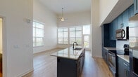 Located near I-435 N in Lenexa, Kansas, this single-floor unit showcases a contemporary design highlighted by dramatically high ceilings that amplify the sense of openness throughout the living areas. Light-toned hardwood flooring flows through the main living and kitchen spaces, creating a warm and cohesive aesthetic.

The kitchen is a standout feature, outfitted with rich navy blue shaker-style cabinetry extending to the ceiling, a classic white subway tile backsplash, stainless steel appliances, and a large center island topped with speckled granite countertops that includes an integrated sink with a matte black faucet. The open-plan layout connects the kitchen seamlessly to the living area, which is bathed in natural light from a wall of oversized windows fitted with horizontal blinds and a glass door leading to an outdoor balcony.

The bedrooms are carpeted for comfort and feature large windows that invite abundant daylight and elevated outdoor views of the surrounding Lenexa neighborhood. Ceiling fans provide additional comfort in both the living area and select bedrooms.

The bathrooms are finished to a high standard, featuring large-format tile surrounds, granite-topped vanities with backlit mirrors, hardwood-style flooring, and frameless glass shower enclosures alongside a soaking tub option. The overall ambiance of the space is bright, clean, and modern.