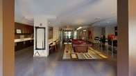 Located at 70 Upper Rock Circle in Rockville, Maryland, this single-floor clubroom serves as a vibrant communal amenity space designed for socializing and recreation. The open-plan layout is anchored by rich hardwood flooring and a warm, contemporary aesthetic throughout.

At the heart of the space sits a full-size billiards table atop a bold geometric area rug, surrounded by ample room for play. Nearby, a Tornado foosball table occupies its own zone, accented by pendant lighting and large-scale artwork that adds an energetic, urban character to the walls.

A stylish bar counter with bar-stool seating lines one side of the room, complemented by dark cabinetry, a flat-screen television, and decorative displays — creating an ideal spot for casual gatherings. The entryway features glass double doors that flood the space with natural light and provide a clean, welcoming transition into the lounge.

A separate dining area offers an octagonal table surrounded by plush leather chairs beneath a distinctive yellow geometric pendant light. Floor-to-ceiling windows in this zone open visually onto an outdoor terrace with patio furniture, seamlessly connecting the interior to the exterior entertaining space. Together, these areas deliver a well-rounded, amenity-rich environment suited for both lively events and relaxed everyday use.