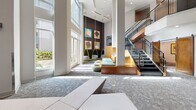 Located at 3011 Hidden Forest Ct in Marietta, GA, this thoughtfully designed communal space offers a dynamic and contemporary environment across a single floor. The grand lobby immediately impresses with its soaring double-height ceilings and floor-to-ceiling windows that flood the interior with abundant natural light, offering views of the surrounding greenery. A striking open staircase with sleek metal railings connects to an upper-level mezzanine, adding architectural depth to the space.

The lounge area is furnished with sculptural, yellow-accented hanging chairs, modular seating, and curated abstract artwork, creating a vibrant yet inviting atmosphere. A textured feature wall with vertical wood slat paneling provides a warm contrast to the cool gray tones throughout. A designated work area with a long desk and mounted display screen offers a functional workspace within the lobby.

The dining area features a row of semi-private booths with tall yellow upholstered banquettes, stone-tiled accent walls, and pendant lantern lighting, providing an intimate setting for casual gatherings. A separate conference room is equipped with a round wood table, modern chairs, a wall-mounted display, and a striking starburst light fixture overhead, making it well-suited for small meetings or collaborative sessions. Patterned carpet flooring unifies the various zones throughout the space.