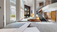 Located at 3011 Hidden Forest Ct in Marietta, GA, this thoughtfully designed communal space offers a dynamic and contemporary environment across a single floor. The grand lobby immediately impresses with its soaring double-height ceilings and floor-to-ceiling windows that flood the interior with abundant natural light, offering views of the surrounding greenery. A striking open staircase with sleek metal railings connects to an upper-level mezzanine, adding architectural depth to the space.

The lounge area is furnished with sculptural, yellow-accented hanging chairs, modular seating, and curated abstract artwork, creating a vibrant yet inviting atmosphere. A textured feature wall with vertical wood slat paneling provides a warm contrast to the cool gray tones throughout. A designated work area with a long desk and mounted display screen offers a functional workspace within the lobby.

The dining area features a row of semi-private booths with tall yellow upholstered banquettes, stone-tiled accent walls, and pendant lantern lighting, providing an intimate setting for casual gatherings. A separate conference room is equipped with a round wood table, modern chairs, a wall-mounted display, and a striking starburst light fixture overhead, making it well-suited for small meetings or collaborative sessions. Patterned carpet flooring unifies the various zones throughout the space.