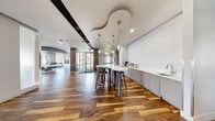 Located at 300 N Mason St in Fort Collins, Colorado, this single-floor clubhouse offers a thoughtfully designed communal space that blends contemporary aesthetics with functional comfort. Rich, multi-tone hardwood flooring flows seamlessly throughout, anchoring the open and inviting atmosphere.

The main common area serves as a central hub, featuring a sculptural, organically shaped ceiling detail adorned with elegant brass pendant lights. A sleek wet bar with light gray cabinetry, a white countertop, and a striking marble-look wall panel provides a refined entertaining station, complemented by a modern high-top island with barstool seating.

The game room is a standout highlight, centered around a contemporary pool table beneath a bold, metallic suspended ceiling element. Large floor-to-ceiling windows flood the space with natural light and offer views of the surrounding Fort Collins streetscape. Lounge seating and bar-height tables complete the social atmosphere.

The living room offers a more intimate retreat, featuring a leather sofa, a round marble coffee table, and a gas fireplace set against a full exposed brick accent wall. A wall-mounted television and large windows with sheer curtains add to its warmth and character. Decorative wooden wall art panels and glass-partitioned entryways add architectural interest throughout the clubhouse.