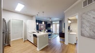This thoughtfully designed single-floor residence offers a seamless open-concept layout connecting the kitchen, dining, and living areas. The kitchen is outfitted with white cabinetry, quartz countertops, stainless steel appliances, and a central island with pendant lighting overhead — ideal for both cooking and casual entertaining. Adjacent to the kitchen, a dedicated dining nook with crown molding and hardwood-style flooring provides an intimate setting for meals. The living room makes a bold statement with a deep navy accent wall, crown molding, a ceiling fan, and French doors that invite natural light and outdoor views. Two well-sized bedrooms each feature plush carpeting, ceiling fans, large windows with views of the surrounding greenery, and ample closet space. One bedroom includes a walk-in closet accessible through its en-suite bathroom. Both bathrooms are finished with white vanities, quartz countertops, soaking tubs, and tiled surrounds. One bathroom showcases a striking teal accent wall, while the other offers a clean, bright aesthetic with hardwood-style flooring. A laundry area is conveniently tucked within the unit. Consistent use of light tones, quality finishes, and thoughtful design details create a cohesive and comfortable living environment throughout.