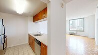 Located on the penthouse level at 225 Grand Street in Jersey City, this one-bedroom, one-bathroom residence offers a well-organized layout across a single floor. The combined kitchen and living area serves as the heart of the home, featuring a peninsula with a stainless steel sink and stone-style countertops that overlook the kitchen. The kitchen is equipped with warm wood cabinetry, stainless steel appliances including a refrigerator, range, and microwave. Large floor-to-ceiling windows in the living area flood the space with natural light and frame impressive views of the Jersey City and lower Manhattan skyline. Parquet hardwood flooring adds warmth and character throughout the living areas. The spacious bedroom is carpeted and also benefits from large windows with sweeping city views, complemented by a wall-mounted HVAC unit. A generously sized walk-in closet with dual wire shelving racks provides ample storage. The bathroom features neutral tile flooring and clean white fixtures, maintaining a simple and functional aesthetic. A hallway connects the main living areas, adding a sense of privacy to the bedroom. The overall ambiance is bright, clean, and urban, well-suited for those seeking a high-floor residence with panoramic city views in downtown Jersey City.