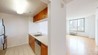 Located on the penthouse level at 225 Grand Street in Jersey City, this one-bedroom, one-bathroom residence offers a well-organized layout across a single floor. The combined kitchen and living area serves as the heart of the home, featuring a peninsula with a stainless steel sink and stone-style countertops that overlook the kitchen. The kitchen is equipped with warm wood cabinetry, stainless steel appliances including a refrigerator, range, and microwave. Large floor-to-ceiling windows in the living area flood the space with natural light and frame impressive views of the Jersey City and lower Manhattan skyline. Parquet hardwood flooring adds warmth and character throughout the living areas. The spacious bedroom is carpeted and also benefits from large windows with sweeping city views, complemented by a wall-mounted HVAC unit. A generously sized walk-in closet with dual wire shelving racks provides ample storage. The bathroom features neutral tile flooring and clean white fixtures, maintaining a simple and functional aesthetic. A hallway connects the main living areas, adding a sense of privacy to the bedroom. The overall ambiance is bright, clean, and urban, well-suited for those seeking a high-floor residence with panoramic city views in downtown Jersey City.