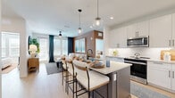 Located in Palm Harbor, Florida, this well-appointed two-bedroom, two-bathroom residence offers a thoughtfully designed single-floor layout with a bright, open-concept living space. Light wood-tone flooring flows throughout, complementing a clean, contemporary aesthetic.

The kitchen is a standout feature, boasting white shaker cabinetry extending to the ceiling, stainless steel appliances including a refrigerator, microwave, and range, and a large center island with quartz countertops and seating for multiple guests. Globe pendant lights add a modern touch overhead.

The open living room features a warm accent wall, a ceiling fan, and large windows and a glass door that invite abundant natural light and provide direct access to the balcony. The primary bedroom is generously proportioned, featuring a textured accent wall, windows with outdoor views, and a spacious walk-in closet with built-in hanging storage. Both bathrooms are clean and functional, with one including a tub-shower combination and warm wood vanity cabinetry.

Additional highlights include three closets for ample storage and a dedicated laundry room equipped with a full-size Whirlpool washer and dryer. The overall design balances modern finishes with warm, inviting tones throughout.