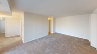 This single-floor residential unit offers a practical and well-organized layout across several distinct living areas. The spacious living room is finished with neutral-toned carpet and features large sliding glass doors that open to a balcony, allowing natural light to fill the space and offering views of surrounding greenery. The galley-style kitchen is outfitted with warm wood cabinetry, white appliances including a range and refrigerator, and light countertops. It opens directly into a dedicated dining nook, which is accented by a chandelier and a window that brings in additional natural light. The bedrooms are carpeted and finished with neutral walls, providing a calm and versatile environment. Each bedroom includes a standard closet with a hanging rod for storage. Two bathrooms serve the unit; one features a tub-and-shower combination with full taupe square tile surround, while the second bathroom also includes a tiled tub-and-shower combination with light blue tile. Throughout the unit, clean white trim and light-colored walls create a bright, cohesive aesthetic that lends itself well to a variety of interior styles.