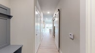 This single-floor unit presents a clean, contemporary design characterized by light hardwood-style flooring, neutral gray walls, and white trim that carry consistently throughout the space. The hallway serves as the central spine of the unit, lined with paneled white doors and a notable sliding barn door with black hardware, adding a modern farmhouse accent. Recessed lighting illuminates the corridor, which leads toward a bright balcony access point at its end.

The open-concept kitchen and living area forms the heart of the unit. The kitchen is well-appointed with gray shaker-style cabinetry, granite countertops, and a full suite of stainless steel appliances, including a range, microwave, and refrigerator. A peninsula with an undermount sink provides additional workspace and casual seating potential, while pendant lighting adds a stylish focal point overhead. A glass-panel door in the kitchen opens directly to a private balcony with outdoor views.

The living area connects seamlessly to the kitchen through a distinctive half-wall pass-through opening, creating visual continuity while defining each zone. A ceiling fan serves the living space. The bathroom features matching granite countertops, gray cabinetry, light flooring, and a tiled shower, maintaining the cohesive aesthetic found throughout the unit.