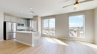 Located along the vibrant E Camelback Road corridor in Phoenix, AZ, this well-appointed 2-bedroom, 2-bathroom residence offers a thoughtfully designed single-floor layout. The open-concept living and kitchen area serves as the heart of the home, bathed in abundant natural light streaming through large floor-to-ceiling windows that frame elevated city views. Light wood-tone flooring extends throughout the main living space, complemented by neutral warm-gray walls and a ceiling fan overhead. The kitchen features a central island with a stainless steel sink and white quartz countertop, paired with gray shaker-style cabinetry, a subway tile backsplash, and a full suite of stainless steel appliances including a gas range, microwave, refrigerator, and dishwasher. Both bedrooms are carpeted and generously sized, with the primary bedroom offering dual windows and a ceiling fan. Each bedroom includes a dedicated closet with built-in shelving and hanging rods. The bathrooms are finished with light wood flooring, tiled tub-shower combinations, and clean white vanities. A dedicated laundry area with an in-unit washer adds everyday convenience. The overall aesthetic is clean, modern, and move-in ready.