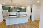 This 1,220-square-foot single-floor residence features 3 bedrooms, 3 bathrooms, 2 closets, and a dedicated laundry room, delivering a functional and thoughtfully designed layout. The kitchen is a standout feature, showcasing sage green shaker-style cabinetry with brass hardware, granite countertops, a beveled subway tile backsplash, stainless steel appliances including a built-in microwave and refrigerator, and light wood-tone flooring that flows throughout the living areas. The combined kitchen and living room creates an open, connected space with access to a private patio overlooking a manicured lawn and a modern multi-story building exterior. The bedrooms feature light hardwood-style flooring, with one room accented by elegant raised panel wainscoting for added architectural character. The primary bedroom measures 170 square feet. The bathrooms are finished with marble-look tile flooring, green vanities with granite countertops, gold hardware accents, globe pendant lighting, and framed mirrors. One bathroom includes a glass-enclosed walk-in shower with subway tile surround, while another features a tub-shower combination. The dedicated laundry room is equipped with a full-size Samsung washer and dryer alongside overhead wire shelving for added storage convenience.