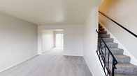 This two-story residence is designed with a practical, open layout that flows naturally between its living spaces. The main level welcomes you through a front entry with a large window that fills the room with natural light. A staircase with decorative wrought-iron railings connects the two floors, adding a subtle architectural detail to the interior.

The main living area is spacious and carpeted in neutral grey tones, opening through an archway into a secondary room featuring sliding glass doors that provide direct outdoor views and ample natural light. Textured ceilings throughout lend a consistent finish to the space.

The kitchen is well-appointed with white cabinetry, dark countertops, stainless steel appliances including a range, microwave, dishwasher, and refrigerator, along with wood-look flooring. Notably, a stacked washer and dryer unit is integrated directly into the kitchen area, offering convenient in-unit laundry.

Upstairs, the bedrooms are carpeted and feature closets with bi-fold doors. One bedroom includes a window with outdoor views, while another sits adjacent to the staircase landing. The bathroom is finished with wood-look flooring, a single vanity with a dark countertop, and a shower-tub combination.