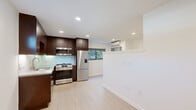 This single-floor unit offers a thoughtfully designed layout that combines functional living spaces with modern finishes throughout. The open-concept kitchen and living area serves as the heart of the unit, where rich dark-espresso cabinetry reaches toward the ceiling, providing ample storage. The kitchen is equipped with a full suite of stainless steel appliances, including a gas range, over-the-range microwave, dishwasher, and a French door refrigerator. A light-toned quartz countertop and a shimmering mosaic tile backsplash add a polished, contemporary touch, while recessed lighting ensures the space is well-lit. Light wood-tone flooring flows seamlessly throughout the unit, creating a bright and cohesive feel. A wall-mounted mini-split system provides climate control in the living area, which benefits from natural light through a window overlooking greenery. The entry area is clean and open, framed by crisp white walls. The bathroom features full-height tile surround, a soaking tub with a glass sliding door enclosure, and a stone-toned vanity with an undermount sink. A mirrored vanity reflects the in-unit washer and dryer conveniently tucked nearby. Overall, the unit presents a clean, modern aesthetic with quality finishes and practical amenities.