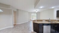 Located at 200 Dahlia Lane in Fort Myers, Florida, this single-floor, 4-bedroom, 2-bathroom home offers a practical and well-appointed layout designed for comfortable living. The open-concept kitchen is a standout feature, showcasing rich dark cabinetry, granite countertops, stainless steel appliances including an electric range and microwave, a deep stainless sink, and a peninsula with bar seating — ideal for casual dining or entertaining. The living areas are finished with neutral-toned large-format tile flooring, while the bedrooms feature warm wood-look laminate flooring and ceiling fans, creating an inviting atmosphere throughout. Several bedrooms include built-in closets, and one bedroom offers a window with a view of the surrounding Florida landscape with palm trees visible outside. The primary bathroom is generously sized, featuring dark vanity cabinetry with granite countertops, a large mirror with vanity lighting, a walk-in glass-enclosed shower, and light tile flooring. The secondary bathroom mirrors the design language with a dark vanity, granite countertop, and tile floors. A dedicated walk-in closet with wire shelving provides ample storage. The home's cohesive neutral palette and consistent finishes create a clean, modern ambiance throughout.