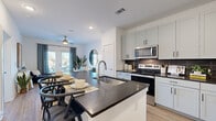 This single-floor residence offers a thoughtfully designed open-concept layout that seamlessly connects the kitchen, dining, and living areas. The kitchen is a standout feature, equipped with white shaker cabinetry accented by matte black hardware, dark granite countertops, a full suite of stainless steel appliances including a refrigerator, electric range, microwave, and dishwasher, and a dark tile backsplash. A generous center island with an integrated sink provides additional prep space and doubles as a casual dining area.

The living room is bright and inviting, benefiting from natural light streaming through French doors that open to a private balcony with outdoor views. A ceiling fan overhead and light wood-look flooring underfoot contribute to the comfortable, airy atmosphere throughout the main living space.

The two bedrooms are well-proportioned and serene, each featuring ceiling fans, plush carpeting, and large windows that allow ample natural light. The bathroom is clean and functional, featuring a full soaking tub with shower combination, a dual-sink vanity with matching dark countertops and white cabinetry, and light wood-look flooring. The overall aesthetic is modern and cohesive, with a neutral palette throughout.