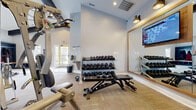 Located at 1038 Bayridge Dr in Lewis Center, Ohio, this fitness center offers a well-appointed workout facility designed to support a comprehensive exercise routine. The space is organized across a single floor and features high ceilings that contribute to an open, airy atmosphere, complemented by light-toned walls painted in a soft blue-gray palette that creates a clean and motivating environment. Recessed lighting and wall-mounted sconces provide ample illumination throughout.

The main workout area is equipped with a multi-station cable machine for strength and resistance training, a three-tier dumbbell rack stocked with a wide range of free weights, kettlebells, and an adjustable workout bench — offering users the tools needed for both targeted and full-body training. A large framed mirror along one wall enhances the sense of space while allowing users to monitor their form. A wall-mounted flat-screen TV adds an entertainment element to workouts.

The facility includes a dedicated entry area with a water fountain and access to natural light through a glass-paneled door, providing a welcoming transition into the space. Neutral, textured flooring ties the room together, balancing functionality with a polished aesthetic. Overall, this fitness center provides a practical, well-maintained environment suited for a variety of fitness goals.