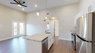 This well-designed 1-bedroom, 1-bathroom unit combines modern finishes with functional living across a single floor. The open-concept living area greets you with notably tall ceilings, recessed lighting, and hardwood-style flooring that extends throughout the main space. Large windows and a glass door fill the area with natural light, offering views of the surrounding neighborhood. A classic white-spindle staircase railing adds a refined architectural detail to the entryway.

The kitchen serves as the centerpiece of the unit, anchored by a generous island topped with light granite countertops and fitted with an undermount sink and pendant lighting above. White shaker cabinetry lines the walls, complemented by a full suite of stainless steel appliances including a range, microwave, dishwasher, and refrigerator. A dedicated laundry area with a full-size washer and dryer adds everyday convenience.

The bedroom features vaulted ceilings that enhance the sense of volume, plush carpeting, and multiple windows that invite abundant natural light and neighborhood views. The bathroom is finished with classic black-and-white mosaic tile flooring, a walk-in shower with white tile surround, and a white vanity topped with granite.
