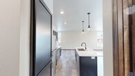 This two-story, two-bedroom, two-bathroom home delivers a thoughtfully designed layout spread evenly across two floors. The main level opens through a welcoming entrance into a combined kitchen and living area that serves as the heart of the home. The kitchen is a standout feature, showcasing dark cabinetry with sleek hardware, white quartz countertops, stainless steel appliances, and a central island with an undermount sink and matte black faucet. Stylish pendant lights hang above the island, adding a contemporary touch. Light wood-look flooring flows throughout the main level, complementing the neutral color palette and allowing natural light from multiple windows to brighten the space. A convenient half bathroom and dedicated laundry room with full-size washer and dryer hookups round out the first floor. Upstairs, the spacious primary bedroom offers a generous footprint, a ceiling fan, and natural light from a corner window. It is complemented by a private bathroom with a walk-in closet featuring built-in shelving, providing ample storage. The second bedroom is bright and well-sized, also benefiting from natural light. Soft carpet flooring on the upper level adds warmth and comfort throughout the sleeping areas.