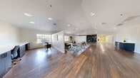 This expansive single-floor amenity center offers a comprehensive and thoughtfully designed community experience across nine distinct areas. The grand entrance greets visitors with striking stained glass double doors, rich hardwood flooring, and recessed lighting that sets an inviting tone throughout.

The main clubroom is a standout space, offering an open, airy layout with vaulted ceilings, abundant natural light from multiple windows, and rich dark hardwood floors. It features distinct seating arrangements including a casual lounge area with mid-century modern furnishings and a separate dining nook, as well as a built-in dark shelving display wall.

A bright hallway with light hardwood flooring leads to additional rooms, including a well-appointed kitchenette featuring white quartz countertops, dark cabinetry, a tile backsplash, and a sink — ideal for catered events or community gatherings. Adjacent spaces include a dedicated fitness room outfitted with cardio and strength-training equipment atop durable rubber flooring, and a fully tiled pet grooming room with a stainless steel wash station.

The mail and parcel room provides organized package management with built-in mailboxes and parcel lockers. Additional flex rooms feature plush carpet, ceiling fans, crown molding, and natural light, offering versatile spaces for a variety of uses.