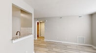 This thoughtfully designed one-bedroom, one-bathroom unit offers a practical and modern living experience across a single floor. Light wood-tone flooring runs consistently throughout the space, providing warmth and visual continuity between rooms.

The open living area is finished with neutral gray walls and clean white trim, creating a bright and versatile backdrop. A pass-through counter with granite-look surfaces connects the living area to the kitchen, which features white shaker-style cabinetry with brushed hardware, a classic white subway tile backsplash, granite countertops, and stainless steel appliances including a refrigerator and dishwasher. Overhead lighting illuminates the galley-style kitchen efficiently.

The bedroom offers a comfortable footprint with a window fitted with blinds that allows natural light to filter in, neutral toned walls, and a closet accessible through a paneled door. The bathroom includes a full soaking tub and shower combination with a curtain rod, a toilet, and a towel bar with brushed gold accents.

A connecting hallway provides access to the utility room, which houses a water heater, keeping functional elements neatly separated from living spaces. The overall design is clean, modern, and move-in ready, with consistent finishes throughout that lend the space a cohesive and polished aesthetic.