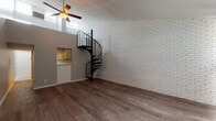 Located at 100 State St in North Haven, Connecticut, this two-floor loft-style space blends industrial character with modern finishes throughout. The main living area makes an immediate impression with its soaring vaulted ceilings, a full white-painted brick accent wall, and rich dark hardwood-style flooring that extends across both levels. A bold black wrought-iron spiral staircase serves as a central architectural focal point, connecting the two floors with a sculptural elegance. Natural light filters in through elevated windows, enhancing the open and airy feel of the space. A ceiling fan provides both function and style overhead.

The kitchen is well-appointed with crisp white shaker-style cabinetry, granite countertops, stainless steel appliances including a range and dishwasher, and a functional layout that maximizes workspace. The bathroom features a tub-shower combination with distinctive dark stone-look tile surround, complemented by the continued white brick wall detail that carries throughout the space, lending a cohesive industrial aesthetic. The upper floor, accessible via the spiral staircase, offers additional living space with vaulted ceilings and wood-style flooring. Overall, this space offers a distinctive loft atmosphere that artfully balances urban industrial design with comfortable, modern living.