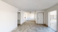 This single-floor residence presents a clean, modern aesthetic defined by a crisp white palette and light wood-look flooring that flows throughout the main living areas. The open living room is spacious and airy, featuring a ceiling fan, a textured ceiling, and a front entry door flanked by large vertical-blind windows that allow natural light to fill the space. A secondary room off the main living area offers the same wood-look flooring and a similarly bright, open feel.

The kitchen has been thoughtfully updated with white shaker-style cabinetry, brushed nickel hardware, stone-look countertops, and a herringbone tile backsplash. Stainless steel appliances — including a refrigerator, range, microwave, and dishwasher — complete the functional and stylish cooking space. A window above the counter brings in additional natural light.

The bedroom features plush carpeting, painted block-style walls, and a window with vertical blinds. The bathroom is finished with light wood-look flooring, a white vanity with stone-look countertop, and a tub-shower combination with marble-style tile surround. Throughout the space, the consistent use of white walls, neutral tones, and updated finishes creates a cohesive and move-in-ready environment.