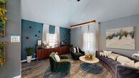This thoughtfully designed single-floor space blends modern aesthetics with warm, eclectic character across several well-defined functional areas. Soaring vaulted ceilings amplify the sense of openness throughout, while large windows dressed in sheer curtains flood the interior with natural light.

The lounge area makes a strong first impression with rich teal accent walls, lush green velvet armchairs, and a plush gray sofa arranged around a marble-topped coffee table. A warm-toned wood credenza lines the back wall, adding a mid-century modern touch, while decorative wall accents and indoor plants contribute to the curated ambiance.

A striking herringbone wood accent wall serves as a dramatic architectural focal point, anchoring a secondary lounge zone and framing a pass-through window that connects to the adjacent areas, reinforcing the open, flowing layout.

The dining area features a round wood table surrounded by teal upholstered chairs, positioned near a compact kitchenette with white cabinetry, a subway tile backsplash, and stainless appliances. Living green wall installations in wooden frames add a vibrant, biophilic design element alongside bold abstract artwork.

A dedicated workspace with a long desk, task chairs, and built-in shelving provides a productive environment. The patterned carpet flooring ties each zone together, creating a cohesive and inviting atmosphere throughout.