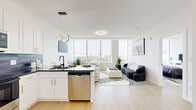 Located at 855 Main St in Bridgeport, CT, this contemporary one-bedroom, one-bathroom residence offers a thoughtfully designed open-concept layout with modern finishes and sweeping city views. Light hardwood flooring flows throughout, complementing the clean, white-walled interior and creating a bright, airy ambiance.

The combined kitchen and living area forms the heart of the home. The kitchen is outfitted with white shaker cabinetry accented by gold hardware, dark granite countertops, a gray tile backsplash, and a full suite of stainless steel appliances. A central island with pendant lighting provides additional prep space and casual seating. The living area benefits from expansive floor-to-ceiling windows that bathe the space in natural light and frame panoramic views of the Bridgeport skyline.

The spacious bedroom continues the modern aesthetic with large windows offering additional city views, light hardwood floors, and ample room for a full furniture arrangement. A dedicated walk-in closet features built-in shelving and a full-length mirror, providing generous storage solutions.

The bathroom is a design standout, featuring a bold geometric-patterned tile accent wall, a floating white vanity with a black-framed mirror, matte black fixtures, and a full soaking tub with an overhead shower.