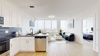 Located at 855 Main St in Bridgeport, CT, this contemporary one-bedroom, one-bathroom residence offers a thoughtfully designed open-concept layout with modern finishes and sweeping city views. Light hardwood flooring flows throughout, complementing the clean, white-walled interior and creating a bright, airy ambiance.

The combined kitchen and living area forms the heart of the home. The kitchen is outfitted with white shaker cabinetry accented by gold hardware, dark granite countertops, a gray tile backsplash, and a full suite of stainless steel appliances. A central island with pendant lighting provides additional prep space and casual seating. The living area benefits from expansive floor-to-ceiling windows that bathe the space in natural light and frame panoramic views of the Bridgeport skyline.

The spacious bedroom continues the modern aesthetic with large windows offering additional city views, light hardwood floors, and ample room for a full furniture arrangement. A dedicated walk-in closet features built-in shelving and a full-length mirror, providing generous storage solutions.

The bathroom is a design standout, featuring a bold geometric-patterned tile accent wall, a floating white vanity with a black-framed mirror, matte black fixtures, and a full soaking tub with an overhead shower.
