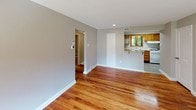 This single-floor home offers a cohesive and functional layout highlighted by warm, polished hardwood flooring that flows throughout the main living areas and bedrooms. The living room is bright and welcoming, featuring a large window that fills the space with natural light and provides views of the surrounding greenery. Neutral gray walls and a textured ceiling complete the clean, understated aesthetic.

The kitchen is well-equipped with abundant warm oak cabinetry, granite-look countertops, and white appliances including a gas range and dishwasher. A skylight overhead floods the space with additional natural light, while a window above the sink overlooks the outdoors. Light gray vinyl flooring in the kitchen provides a practical contrast to the hardwood found elsewhere.

The bedrooms continue the home's consistent design language, each featuring the same rich hardwood floors, neutral walls, and textured ceilings. Multiple windows in each bedroom invite natural light and frame views of mature trees and the surrounding landscape, creating a calm and comfortable atmosphere.

The bathroom showcases a classic black-and-white tile design, with bold black tile borders accenting the crisp white walls and soaking tub. The overall layout of the home is efficiently organized, with a central hallway connecting the living areas, kitchen, and bedrooms seamlessly.