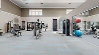 Located at 803 Corday Dr in Naperville, IL, this expansive fitness center offers a generously sized, single-floor exercise space designed to accommodate a full range of workout activities. The facility features soaring ceilings with recessed lighting and a row of transom windows that usher in abundant natural light, creating a bright and energizing atmosphere throughout.

The space is divided into distinct functional zones. A dedicated cardio area houses multiple treadmills and stationary bikes, including upright, recumbent, and spin cycles, complemented by wall-mounted flat-screen televisions. A strength training zone is equipped with a variety of Precor selectorized machines, a multi-functional cable and rack system, a climbing peg board, and an organized storage unit for medicine balls and exercise accessories.

Large floor-to-ceiling mirrors line one wall, visually expanding the space and supporting proper form during workouts. The flooring transitions between patterned low-pile carpet and smooth hard surface areas suited for dynamic movement. Tasteful wall art featuring nature-inspired motifs adds a calming aesthetic contrast to the energetic environment. Built-in storage shelving near the entrance provides organization for smaller fitness accessories, rounding out this well-appointed and comprehensive fitness facility.