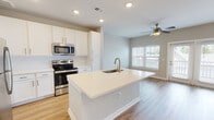 Located at 1001 Cox Grade Rd in Panama City Beach, Florida, this single-floor residence offers a bright, contemporary living experience with a thoughtfully designed open-concept layout. The kitchen is a standout centerpiece, featuring crisp white shaker cabinetry, a classic subway tile backsplash, a full suite of stainless steel appliances including a refrigerator, range, and built-in microwave, and a generously sized island with a light quartz countertop and an integrated gold-toned sink — ideal for both meal preparation and casual dining. Recessed lighting throughout the kitchen ensures a well-lit, inviting atmosphere.

The adjoining living area is finished with warm wood-look luxury vinyl plank flooring and is illuminated by natural light streaming through multiple windows with classic blinds. French doors open to a private outdoor area, extending the living space and providing a seamless indoor-outdoor connection. A ceiling fan adds both function and style to the main living space.

The bedroom is carpeted for comfort, benefits from natural light through a large window, and includes its own ceiling fan. The bathroom is cleanly appointed with wood-look flooring, a white shaker vanity with quartz countertop, gold hardware accents, and a full tub-shower combination with tiled surround. The overall aesthetic throughout is clean, modern, and move-in ready.