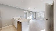 This well-designed 2-bedroom, 2-bathroom single-floor residence offers a clean, contemporary aesthetic throughout. The open-concept layout connects the kitchen and living area seamlessly, creating an efficient and inviting shared space. The kitchen features sleek white cabinetry, white quartz countertops, stainless steel appliances including a refrigerator and dishwasher, and a peninsula with an undermount sink — ideal for both cooking and casual dining.

The living area is bright and airy, benefiting from large windows that invite generous natural light and provide views of the surrounding greenery. A wall-mounted mini-split system provides climate control, complemented by baseboard heating in the bedrooms. Light wood-toned flooring runs throughout the main living spaces and bedrooms, contributing to the home's modern, cohesive feel.

Both bedrooms are well-proportioned and bright, with the primary bedroom featuring a large window with outdoor views and ample room for furnishings. Each bedroom is served by a dedicated closet for storage convenience.

The two bathrooms are finished in a modern style — one features a floating white vanity with an undermount sink, a round black-framed mirror, and access to a closet, while the other includes a glass-enclosed walk-in shower. Soft grey walls throughout the home tie each room together with a calm, neutral palette.