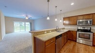This 2-bedroom, 2-bathroom home offers a thoughtfully designed single-level layout that maximizes comfort and functionality. The open-concept kitchen and living area serves as the heart of the home, featuring rich cherry wood cabinetry, granite countertops, and stainless steel appliances including a range, microwave, and dishwasher. A peninsula with pendant lighting provides both additional workspace and a natural division between the kitchen and the carpeted living room. The living room is generously sized, finished with plush carpet, a ceiling fan, and sliding glass doors that open to views of a green, landscaped yard. Natural light flows freely throughout the space. The primary bedroom offers a comfortable footprint with carpeted flooring, a window for natural light, and access to a walk-in closet equipped with wire shelving systems for organized storage. The bathrooms are clean and functional, featuring tub-shower combinations with brushed nickel fixtures. Two entrance points add convenience, while a hallway connects the rooms efficiently. The exterior includes a concrete driveway, a white vinyl privacy fence, and open green surroundings with views of a quiet residential neighborhood, contributing to a peaceful and private atmosphere.