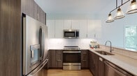 This single-floor residence in Framingham, MA offers a thoughtfully designed layout with modern finishes throughout. The contemporary kitchen is a standout feature, showcasing a two-tone cabinetry scheme with dark wood lower cabinets and crisp white upper cabinets, complemented by a classic white subway tile backsplash. Stainless steel appliances — including a French door refrigerator with ice and water dispenser, an electric range, over-the-range microwave, and dishwasher — complete the well-appointed kitchen. Warm-toned hardwood-style flooring runs throughout the space, adding continuity and warmth.

The bedrooms are bright and airy, each featuring large grid-pane windows that frame lush, tree-filled outdoor views, flooding the rooms with generous natural light. The clean white walls and open floor space provide a versatile canvas for a variety of layouts.

Two bathrooms serve the residence. A half bath features a single-sink vanity with white countertop, gray cabinetry, and a framed mirror. The full bathroom includes a glass-door walk-in shower, a matching vanity, and the same light hardwood-style flooring. Both bathrooms maintain a clean, minimalist aesthetic consistent with the rest of the home. The overall ambiance is modern, bright, and move-in ready.
