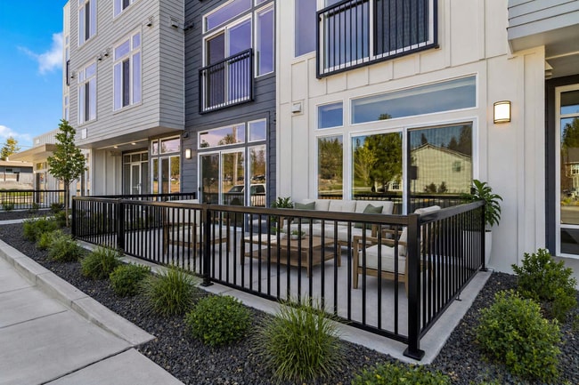 Modern apartment exterior featuring a stylish patio with cozy seating, surrounded by lush greenery for a relaxing outdoor experience. - Lofts at Garden District