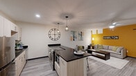 Located at 315 Dayton St in Hamilton, Ohio, this well-designed one-bedroom, one-bathroom residence offers a thoughtfully laid-out floor plan across a single level. The open-concept living and kitchen area forms the heart of the home, where a bold golden-yellow accent wall adds a vibrant focal point to the living space, complemented by grey wood-style flooring and a ceiling fan overhead. A sleek sliding barn door provides stylish access to the bedroom area.

The kitchen is a standout feature, showcasing light wood cabinetry topped with dark granite countertops, stainless steel appliances including a range and refrigerator, and a generous island with bar seating. Industrial-style pendant lighting adds a modern touch above the island and throughout the open area.

The bedroom is a calm, neutral retreat with elevated ceilings, a built-in closet, and a window that brings in natural light. The bathroom is clean and contemporary, featuring a frameless glass walk-in shower with subway tile, a single-sink vanity with light wood cabinetry, and a large mirror. Throughout the unit, consistent grey wood-style flooring and neutral wall tones create a cohesive, modern aesthetic.