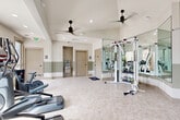 Located at 10571 Colorado Blvd in Thornton, CO, this fitness center offers a thoughtfully designed workout space spread across a single floor. The room features vaulted ceilings that lend an open, airy feel, complemented by recessed lighting and dual ceiling fans that ensure comfortable air circulation throughout. Large arched and standard windows invite natural light, providing views of the surrounding outdoor greenery.

The gym is outfitted with a comprehensive selection of equipment to support both cardio and strength training goals. Cardio offerings include treadmills, ellipticals, stair climbers, and stationary bikes, several positioned on turf sections for added stability. A cable resistance machine and TRX suspension training system cater to full-body strength workouts, while a dedicated dumbbell rack and plyo boxes support functional fitness routines. Full-length mirrored wall panels visually expand the space and assist users in monitoring their form.

The light-toned tile flooring and neutral two-tone wall design — soft sage green along the lower half and crisp white above — create a clean, modern aesthetic. A water fountain is conveniently accessible near the restroom doors, adding practical amenities to the overall experience. This fitness center delivers a well-rounded, professional workout environment suited for a variety of fitness levels and training styles.