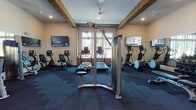 Located in Matthews, NC, this well-appointed fitness center at Glenloch Creek offers a comprehensive workout environment designed to accommodate a wide range of exercise needs. The space features soaring ceilings with distinctive wood beam accents and recessed lighting, creating an open and energizing atmosphere throughout.

The cardio zone is anchored by multiple treadmills, elliptical trainers, recumbent and upright stationary bikes, and a seated stepper, all positioned near large multi-pane windows that flood the area with natural light and provide pleasant outdoor views. Wall-mounted flat-screen televisions are strategically placed to keep members engaged during workouts.

The strength training area is equally well-equipped, featuring a cable/pulley multi-functional machine, a full dumbbell rack ranging across a broad spectrum of weights, and a flat weight bench. Floor-to-ceiling mirrors line the walls, visually expanding the space and allowing users to monitor their form throughout their routines.

Additional amenities include a shelving unit stocked with towels and essentials near the glass entry doors, and dark, patterned carpet flooring that defines the workout zones. The overall design balances functionality with a modern aesthetic, making this fitness center a practical and inviting facility for residents of the Glenloch Creek community.
