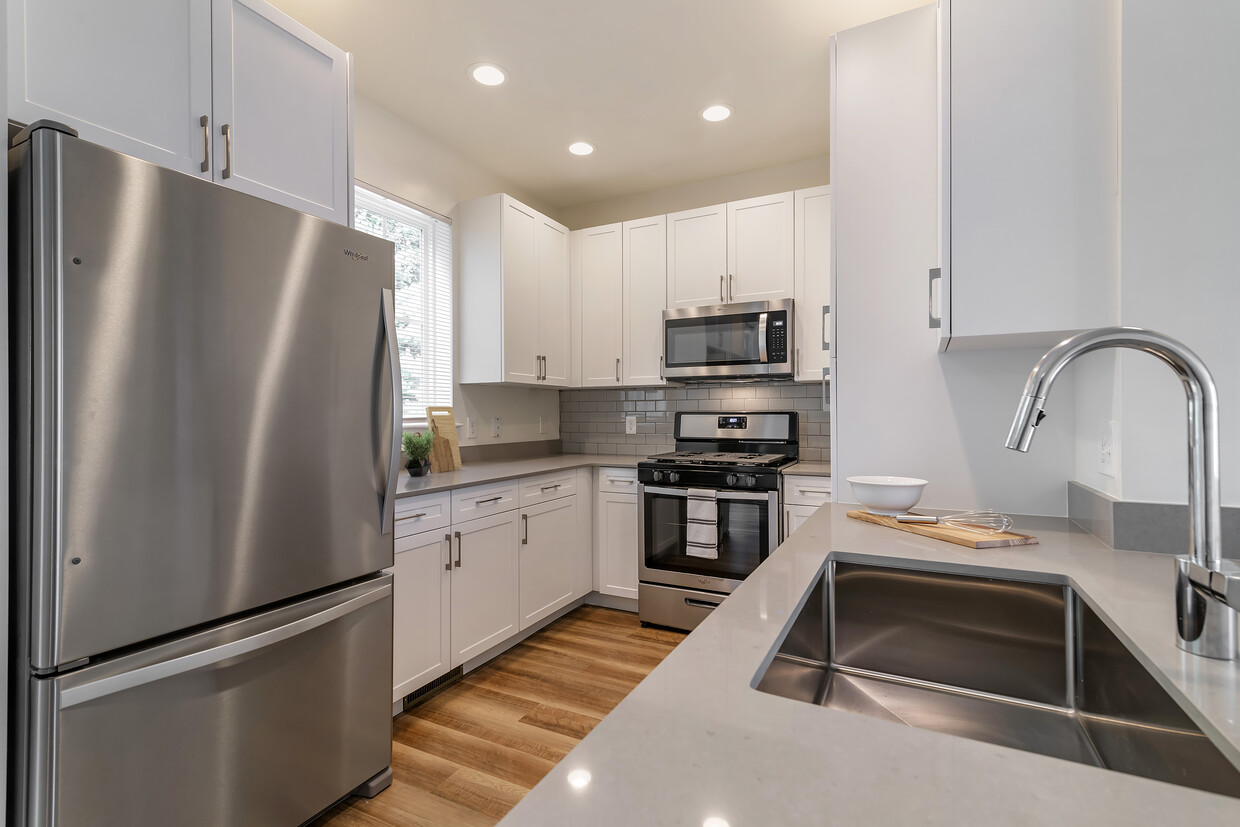 Cocina renovada del Paquete II con gabinetes blancos, encimeras de cuarzo gris, salpicadero de azulejos de metro gris, electrodomésticos de acero inoxidable y pisos de superficie dura - Avalon Northborough