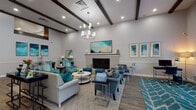 Located at 5039 Chalet Ct in Tampa, Florida, this single-floor residence offers a well-organized layout designed for comfortable everyday living. The living room serves as the heart of the home, featuring warm hardwood-style flooring, a textured ceiling, and a ceiling light fixture. Sage-green walls and tropical botanical wall art lend the space a relaxed, nature-inspired atmosphere, complemented by a mix of seating and a mid-century modern coffee table. An adjacent sitting area provides additional lounging space, complete with hardwood floors, neutral tones, and a large wall-mounted television. The dining area features hardwood-style flooring, chair rail molding, and a sliding door that introduces natural light, creating a bright and welcoming space for meals. The kitchen is outfitted with white cabinetry, dark granite-style countertops, a decorative tile backsplash, and stainless steel fixtures, offering a clean and functional workspace. The bedrooms are carpeted for comfort; one features dual windows that fill the room with natural light and a ceiling fan, while another showcases a bold teal accent wall adorned with gold palm leaf décor, adding a distinctive design touch. Throughout the home, a cohesive nature-inspired color palette, consistent trim work, and thoughtful styling create a warm and inviting overall ambiance.