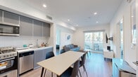 Located at 5460 Fountain Ave in the heart of Los Angeles, this modern single-floor unit offers five bedrooms and four bathrooms thoughtfully arranged across a well-designed floor plan. The open-concept living and dining area serves as the social hub of the space, featuring warm hardwood-style flooring, recessed lighting, and large sliding glass doors that open to a private balcony overlooking lush cypress trees. The kitchen is outfitted with sleek gray cabinetry, white countertops, a textured tile backsplash, and stainless steel appliances including a gas range, dishwasher, and microwave. The dining area adjoins the kitchen seamlessly, providing ample space for a full-sized table and chairs. The living room offers a comfortable seating arrangement, a wall-mounted flat-screen TV, and direct balcony access, filling the space with natural light. Each of the five bedrooms features clean white walls, hardwood-style flooring, and windows that bring in natural light. The four bathrooms are finished with large-format tile flooring, modern gray vanities with mirrored medicine cabinets, and glass-enclosed showers. Long, well-lit hallways with recessed lighting connect the rooms efficiently, contributing to the unit's clean, contemporary aesthetic throughout.