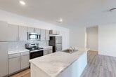 This single-story residence offers a well-designed layout comprising three bedrooms, two bathrooms, a dedicated laundry room, a closet, and a connecting hallway. The open-concept kitchen and living area serves as the centerpiece of the home, featuring a large island with a striking marble-style countertop and an integrated sink. The kitchen is equipped with stainless steel appliances, including a refrigerator, electric range, and microwave, complemented by sleek gray cabinetry and a classic white subway tile backsplash. Wood-look hard flooring runs throughout the main living and kitchen areas, contributing to a clean, contemporary aesthetic.

The living area benefits from natural light through windows and a glass door, creating a bright and welcoming atmosphere. The bedrooms are carpeted for comfort, each featuring a ceiling fan and windows that allow for natural light. The hallway connects the private areas efficiently, with a closet providing additional storage.

The bathrooms are finished in a clean, minimalist style, with one featuring a full tub-shower combination. The dedicated laundry room includes an in-unit washer and dryer with overhead shelving. Throughout, the design emphasizes a modern, functional, and cohesive aesthetic.