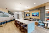 Located at 2501 Gunbarrel Rd in Chattanooga, TN, this thoughtfully designed community amenity space spans a generous single floor and seamlessly blends social, recreational, and relaxation zones into one cohesive environment. Light wood-look flooring flows throughout, unifying the distinct areas while complementing a warm, contemporary aesthetic.

The central social hub features a striking marble-topped island with a decorative blue base, illuminated by oversized circular pendant lights. Built-in banquette seating lines the walls, accompanied by bistro-style tables and upholstered chairs, ideal for casual gatherings. A postcard-inspired mural adds a local Chattanooga character to the backdrop.

The lounge area offers a plush sectional sofa, accent chairs in rich tones, layered area rugs, and a large-screen TV mounted within a textured feature wall. Circular halo pendants overhead reinforce the modern design language, while open shelving with decorative accessories adds warmth.

The game room includes a full-size pool table, a shuffleboard table, and wall-mounted displays showcasing virtual fireplaces. Generous windows invite natural light and views of the surrounding community. Additional seating nooks with orange accent chairs provide quieter retreat spots, while the overall space maintains an energetic yet inviting ambiance throughout.