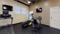 Located at 10824 Lindbrook Dr in Los Angeles, CA, this fitness center is a fully equipped, single-floor workout facility designed to support a wide range of exercise routines. The space features warm beige walls, durable rubber flooring throughout, and an exposed ceiling with industrial-style ductwork and overhead lighting that gives the gym an open, functional feel.

The free weights area is well-stocked with a multi-tier dumbbell rack holding a comprehensive range of weights, complemented by a flat workout bench for strength training. Full-length wall mirrors line this section, enhancing the sense of space and allowing for proper form checks during exercise.

A dedicated cardio zone houses an elliptical trainer, a recumbent bike, and a treadmill, with a wall-mounted flat-screen TV nearby for entertainment during workouts. Natural light filters in through multiple windows fitted with blinds, creating a bright and inviting atmosphere.

The strength training area features a multi-station cable machine, providing options for a full-body workout. A separate open-floor stretching and flexibility area is equipped with stability balls, exercise mats, and foam rollers, with posted workout guides on the wall for reference. The facility also includes convenient access doors and ample open floor space, making it a practical and comprehensive fitness destination.