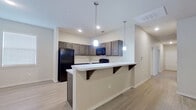 This single-floor residence presents a well-organized layout with distinct living zones connected by consistent neutral-toned finishes throughout. The kitchen serves as a central highlight, showcasing dark espresso-stained cabinetry that extends to the upper walls, providing generous storage capacity. White countertops offer a clean contrast against the cabinetry, while black appliances—including a refrigerator, range, and over-the-range microwave—create a cohesive, modern aesthetic. A peninsula with bracket-supported overhang extends outward, offering casual bar-style seating and a natural transition into the adjacent living area. Pendant lighting drops from the ceiling above the peninsula, adding focused illumination and a polished design detail. Recessed lighting and light wood-style flooring further enhance the open feel of the kitchen and living space. The bedrooms feature soft carpeting, neutral wall tones, and windows fitted with horizontal blinds, allowing for natural light control. One room features light wood-style flooring and a ceiling fan with integrated lighting. Raised panel interior doors with brushed nickel hardware are found throughout, adding a refined touch. The overall ambiance is clean, contemporary, and move-in ready.
