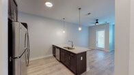 This single-floor residence in St. Peters, Missouri offers a well-designed layout with modern finishes throughout. The kitchen serves as a central focal point, anchored by a large island with light granite countertops and an undermount sink. Dark espresso cabinetry provides striking contrast against the white subway tile backsplash, while stainless steel appliances—including a refrigerator, electric range, and microwave—complete the functional cooking space. Pendant lighting above the island adds warmth and visual interest.

The open living area flows directly from the kitchen, featuring light wood-style flooring and a ceiling fan with integrated lighting. A glass-paneled exterior door fills the space with natural light. The bedroom features plush carpeting and neutral wall tones, creating a calm and comfortable environment. A dedicated walk-in closet provides generous storage with built-in wire shelving across multiple levels.

The bathroom mirrors the kitchen's design language, incorporating matching dark cabinetry topped with granite, an undermount sink, brushed nickel fixtures, and light wood-style flooring. A large mirror and overhead lighting round out this well-appointed space. Throughout, neutral gray walls, clean white trim, and consistent finishes create a cohesive, contemporary aesthetic.