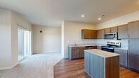 This well-appointed one-bedroom, one-bathroom apartment in Lake Saint Louis, Missouri offers a thoughtfully designed single-floor layout that balances comfort and functionality. The open-concept living and kitchen area forms the heart of the unit, where warm hardwood-style flooring transitions seamlessly into plush carpeting in the living space. The kitchen is outfitted with rich wood cabinetry, granite countertops, a center island, and a full suite of stainless steel appliances including a range, over-the-range microwave, dishwasher, and refrigerator. A dedicated wine rack adds a distinctive touch above the cabinetry. Natural light fills the living area through large windows and a sliding glass door that opens onto a private balcony, offering pleasant outdoor views of the surrounding landscape. The bedroom is generously sized with soft carpeting, a large window, and access to a walk-in closet with built-in shelving for ample storage. The full bathroom features granite countertops, a modern single-basin vanity with a large mirror, wood-tone cabinetry, and a full tub-shower combination. Neutral wall tones and recessed lighting throughout create a clean, contemporary ambiance suited for comfortable everyday living.