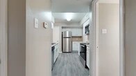 Located at 5975 S Cooper St in Arlington, Texas, this single-floor, three-bedroom, two-bathroom home offers a well-organized layout with a practical mix of living spaces. The kitchen is a standout feature, outfitted with stainless steel appliances including a refrigerator, dishwasher, electric range, and over-the-range microwave. White cabinetry lines the walls and provides ample storage, while light-toned countertops and wood-style vinyl plank flooring complete the clean, modern look. A pass-through counter connects the kitchen to the living area, which features a ceiling fan and a seamless flow between spaces. The living room is carpeted, creating a warm contrast to the hard flooring in the kitchen and hallway. Each bedroom offers carpeted floors, neutral wall tones, and closet space, with the primary bedroom providing a generously sized layout. Two full bathrooms each include a tub-shower combination with white tile surrounds, white cabinetry, and wood-style flooring. A hallway connects the main living areas to the bedrooms and bathrooms. Natural light filters in through multiple windows throughout the home, enhancing the bright and functional ambiance of this well-appointed Arlington residence.