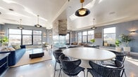 Located at 618 N Third St in Minneapolis's vibrant North Loop neighborhood, this generously sized, single-floor space blends modern sophistication with industrial character. The open-concept main living area features highly polished concrete floors that reflect abundant natural light streaming in through oversized black-framed windows, offering sweeping views of the surrounding cityscape. A striking floor-to-ceiling stacked stone fireplace serves as the architectural centerpiece, anchoring the space and dividing the lounge and dining zones. Stylish pendant lighting with brass and matte black finishes adds warmth and visual interest throughout.

A sleek wet bar with teal hexagonal tile backsplash, white cabinetry, and stainless steel appliances provides a refined entertainment focal point. The dining area accommodates a large round table with woven black chairs, while the lounge area is furnished with plush blue velvet seating. Textured herringbone wallcovering lines the hallway, which leads to an expansive rooftop terrace featuring multiple seating areas, gas grills, planters, and panoramic views of the Minneapolis skyline.

A lower-level area showcases raw exposed brick walls, concrete ceilings with visible ductwork, and dark hardwood floors — ideal for a more intimate, industrial-style gathering space complete with a ping-pong table and bar-height seating.