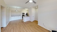 This single-story residence presents a clean, contemporary design centered around an open-concept living and kitchen area. The living space features light wood-look flooring, a vaulted ceiling with a ceiling fan, and a sliding glass door with vertical blinds that fills the room with natural light. A ceiling fan pendant light adds a functional decorative touch to the space.

The kitchen is well-appointed with white shaker cabinetry, gray countertops, a central island, and a full suite of stainless steel appliances, including a refrigerator, range, and microwave. A built-in shelving and cabinet unit adjacent to the kitchen offers additional storage and display space, illuminated by a pendant light overhead.

Multiple bedrooms are carpeted and generously proportioned. The primary bedroom features vaulted ceilings, a ceiling fan, and a window allowing natural light. Additional bedrooms offer large windows with exterior views and ample wall space.

Two bathrooms serve the unit. One includes a tub-shower combo with white tile surround and brushed nickel fixtures. The other features a walk-in glass-door shower, a teal vanity with white countertop, and wood-look flooring, offering a more updated aesthetic. Both bathrooms maintain a clean, neutral palette throughout.